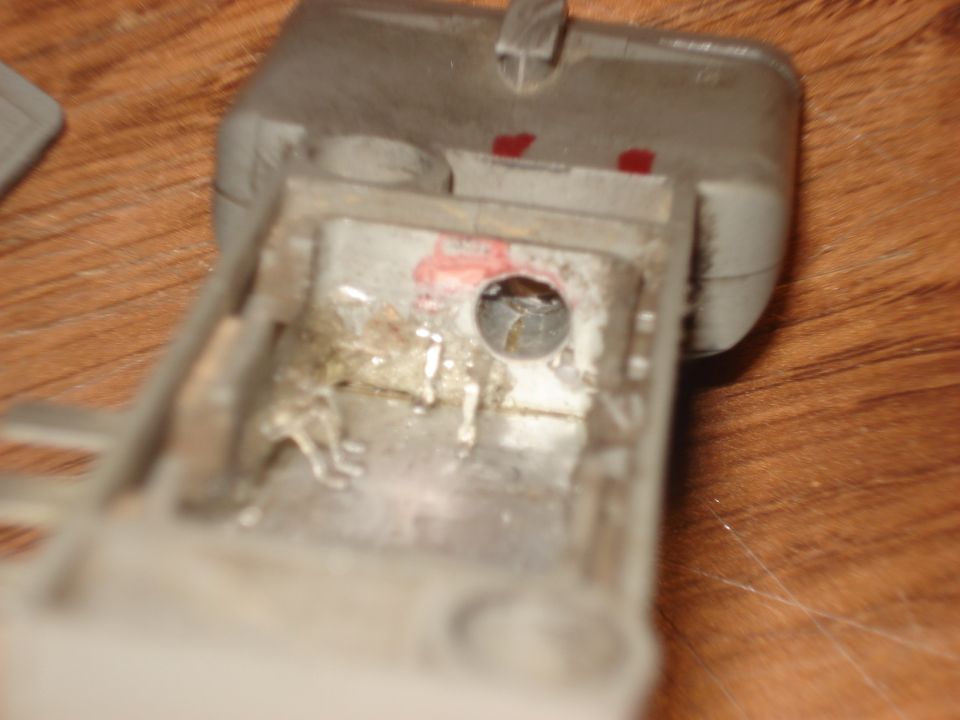 Opened gray relay/switch housing showing corroded burnt internal contacts on wood table