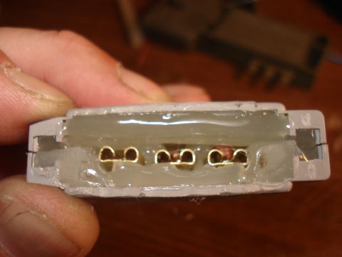 1986 Ford Bronco - A hand holds a white plastic electrical connector with four gold terminals, showing internal wiring connections.