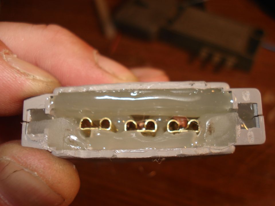 Hand holding six-pin gold-terminal connector housing with silicone potting