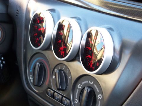 1995 Ford Probe - Close-up of aftermarket gauges and climate controls mounted on a vehicle's dashboard.