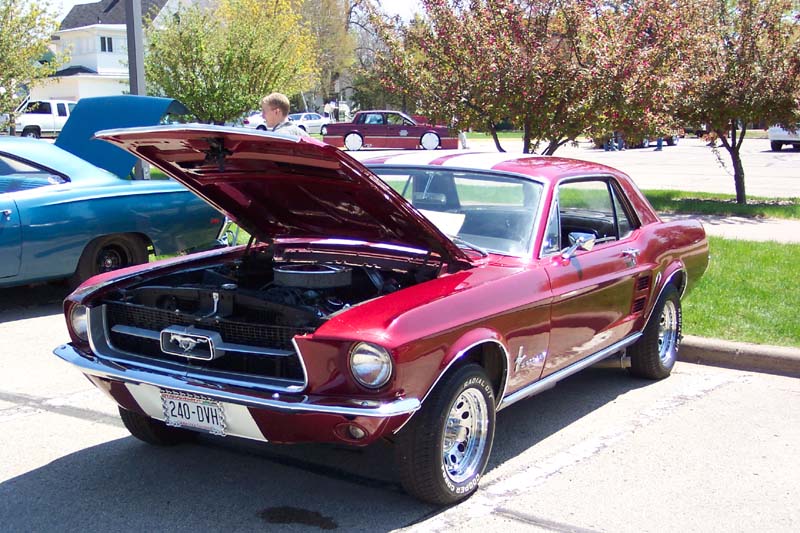 Candy red 1967 Ford Mustang coupe with hood open at an outdoor car show