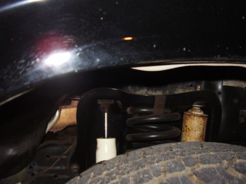 1986 Ford Bronco - Close-up view of the front suspension system of a black vehicle, showing a coil spring and shock absorber.