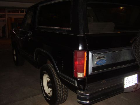 1986 Ford Bronco - Rear view of a black 1986 Ford Bronco, showing its distinctive body style and chrome accents.