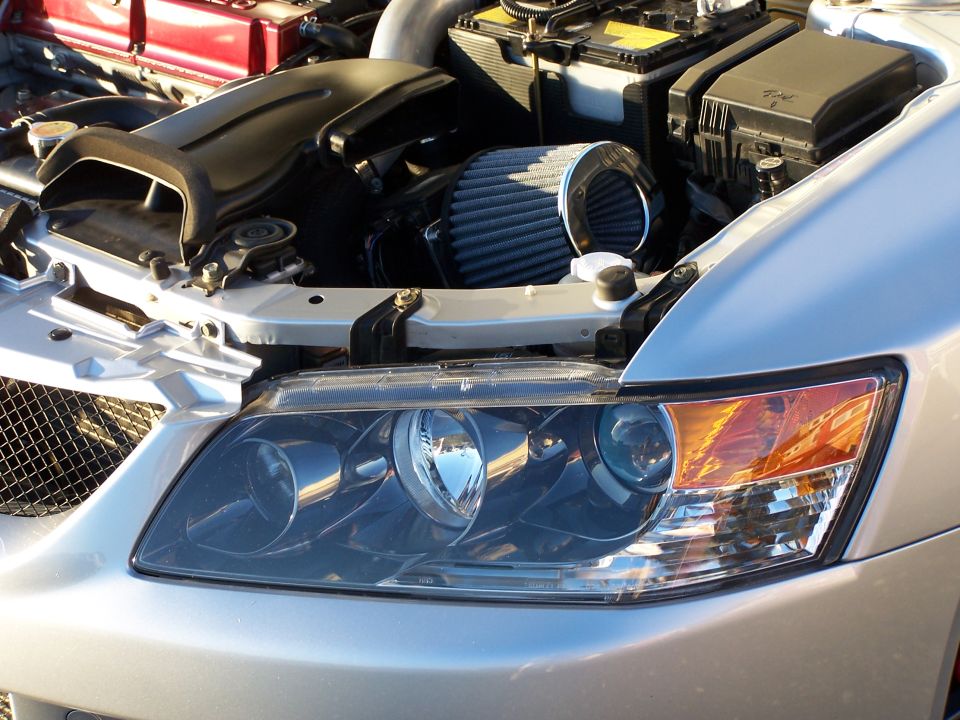 Silver car's engine bay showing air filter, battery, and headlight assembly