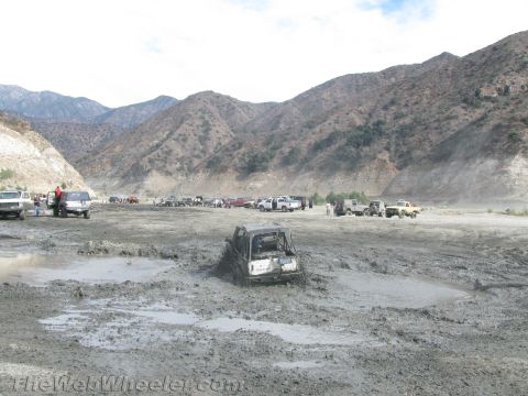 1987 Suzuki Samurai - A group of off-road vehicles are stuck in a muddy terrain, with mountains visible in the distance.