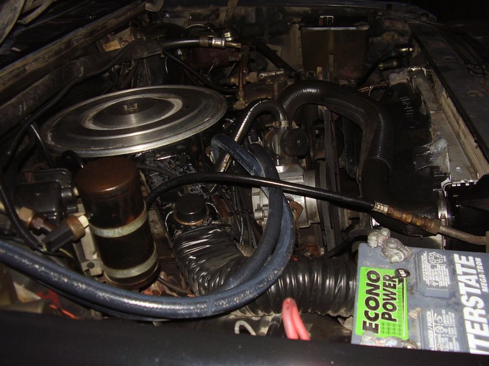 Engine bay showing air filter housing, hoses, battery, and engine components