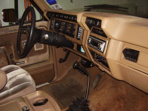 1986 Ford Bronco - The interior of this truck features a tan dashboard with woodgrain accents and a prominent floor shifter.