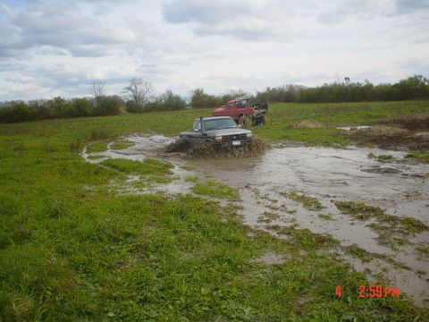 1990 Ford Ranger - Two trucks navigate a muddy field under a cloudy sky.