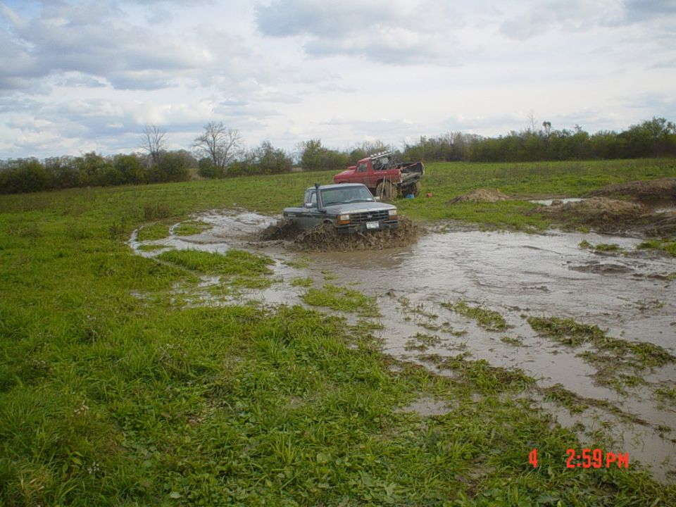 Silver Ford 4x4 pickup plowing through a flooded mud hole in a pasture