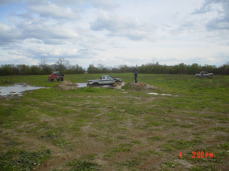 Silver 4x4 pickup crossing a water trench in a field with spectators and other trucks