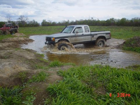 1990 Ford Ranger - A silver pickup truck navigates a water obstacle off-road, with a red vehicle in the distance.