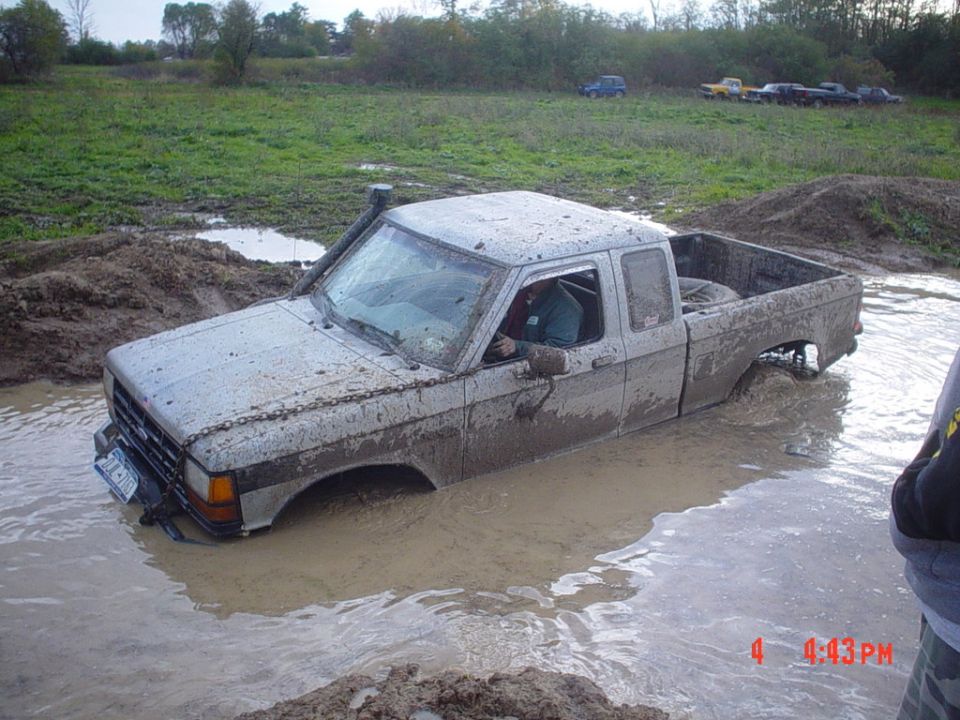 White Ford pickup with snorkel buried to the doors in a muddy water hole