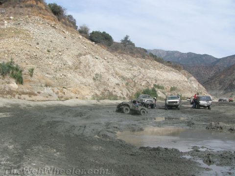 1987 Suzuki Samurai - Off-road vehicles navigate a muddy terrain with a steep, rocky embankment in the background.