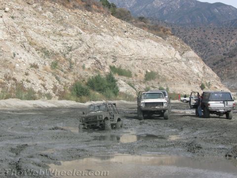 1987 Suzuki Samurai - Multiple 4x4 vehicles navigate a challenging muddy terrain, with one vehicle partially submerged.