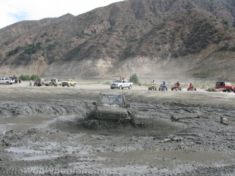 1987 Suzuki Samurai - A 1987 Suzuki Samurai navigates a challenging muddy terrain, with other off-road vehicles and ATVs visible in the background.
