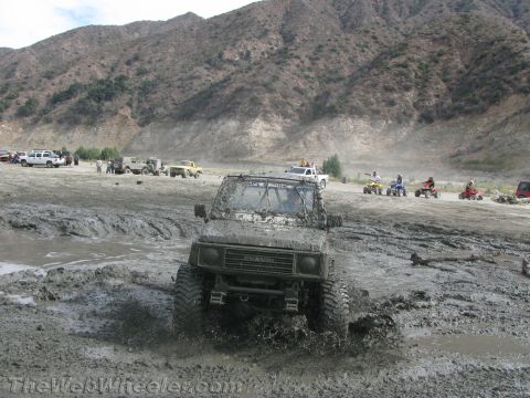 1987 Suzuki Samurai - This Suzuki Samurai navigates a muddy terrain, with other vehicles and ATVs visible in the background.