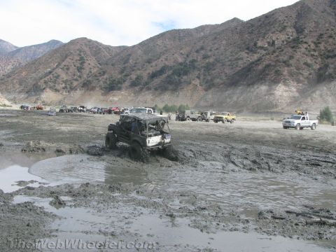 1987 Suzuki Samurai - A group of off-road vehicles navigate a challenging muddy terrain, with a prominent vehicle struggling in the foreground.