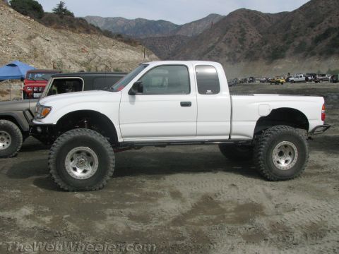 1987 Suzuki Samurai - Modified white pickup truck sits on a dirt lot with mountains in the background.