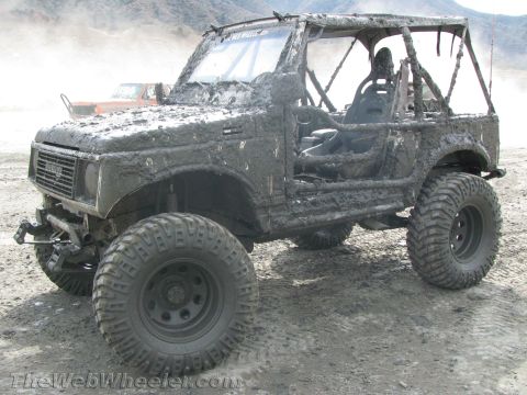 1987 Suzuki Samurai - This heavily modified off-road vehicle is covered in mud after an outing. Another vehicle is visible in the background.