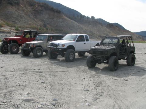 1987 Suzuki Samurai - Four modified off-road vehicles are parked on a dirt lot with a mountainous backdrop.