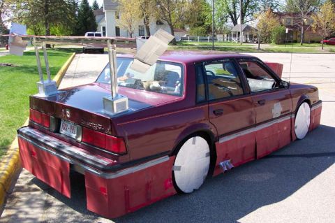 1996 Ford Taurus - This heavily modified sedan features a prominent rear spoiler and extensive red body kit modifications.