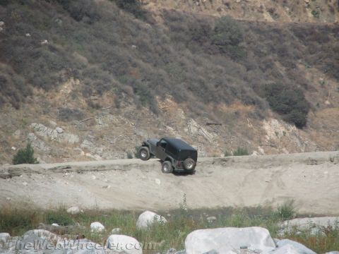 1987 Suzuki Samurai - A black off-road vehicle navigates a dusty trail on a steep, rocky hillside.