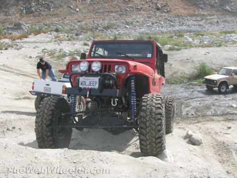 1987 Suzuki Samurai - A modified red Jeep Wrangler is shown off-road with a white pickup and a tan SUV nearby.