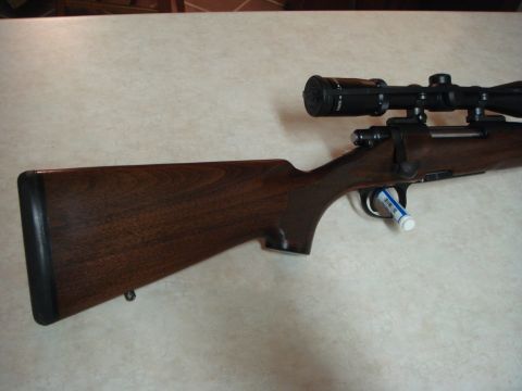 1992 Ford Bronco - Close-up of a rifle's wooden stock and scope, resting on a speckled surface.
