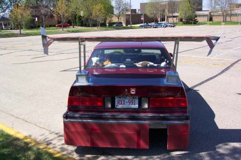 1996 Ford Taurus - A red sedan is seen from the rear, modified with a large spoiler and a custom bumper extension.