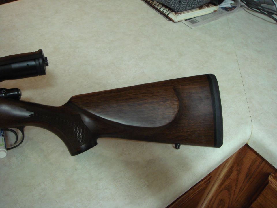 Wooden rifle stock with black scope attached, resting on a table