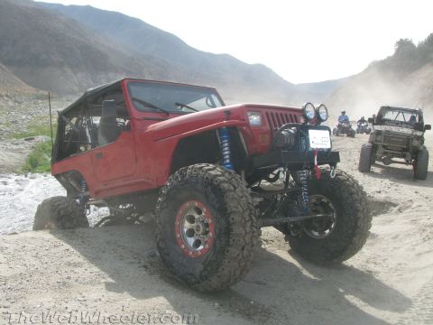 1987 Suzuki Samurai - A modified red Jeep navigates a dusty trail, accompanied by other off-road vehicles in a mountainous landscape.