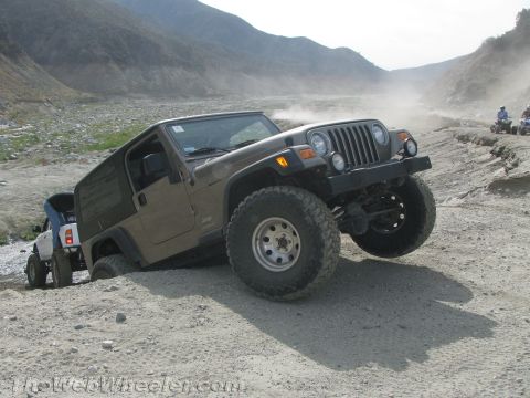 1987 Suzuki Samurai - Two off-road vehicles navigate a dusty, uneven terrain with mountains in the background.