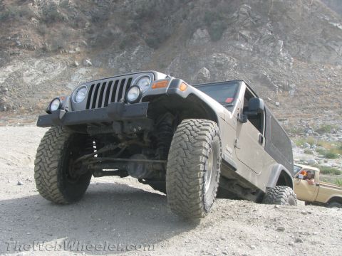 1987 Suzuki Samurai - A Jeep Wrangler TJ navigates a rough, dusty trail with another vehicle visible in the background.