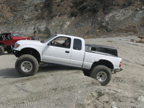 1987 Suzuki Samurai - A white pickup truck is shown off-roading with another vehicle in the background.