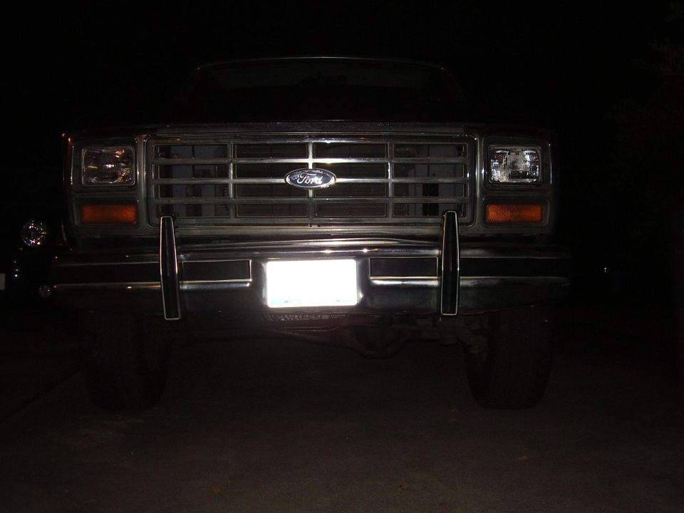 Front view of a Ford truck grille with a blank license plate. The grille has horizontal bars and a Ford emblem