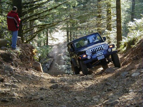 2005 Jeep Wrangler - A black 2005 Jeep Wrangler tackles a challenging, rocky off-road trail in a wooded area.