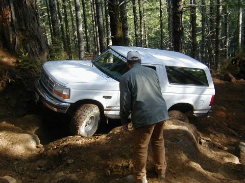 2005 Jeep Wrangler - A white Ford Bronco is shown navigating a challenging off-road trail in a wooded area.