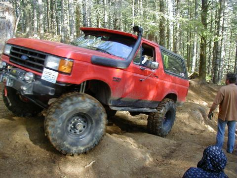 2005 Jeep Wrangler - A red Ford Bronco navigates a challenging off-road trail with a snorkel and oversized tires.