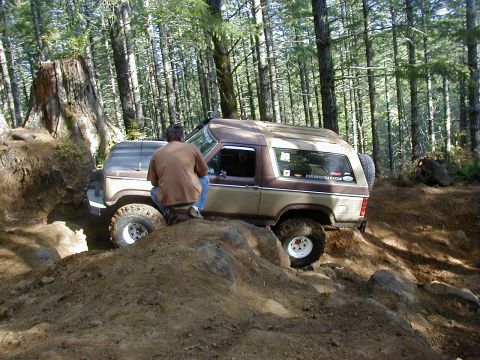 2005 Jeep Wrangler - A two-tone Ford Bronco II navigates a challenging off-road course in a wooded area.