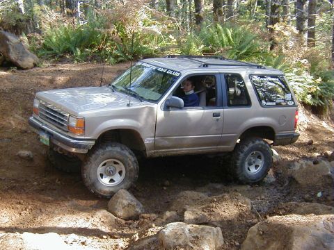 2005 Jeep Wrangler - This tan SUV is navigating a challenging rocky terrain, with text on the windshield indicating membership in the 'BIG BRONCOS 4X4 CLUB'.