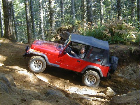2005 Jeep Wrangler - A red Jeep Wrangler navigates a challenging off-road course through a forest.