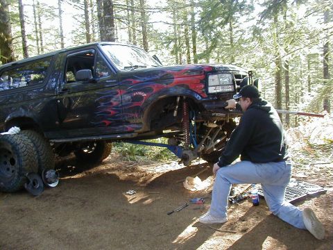 2005 Jeep Wrangler - A person works on the front suspension of a black SUV with flame decals, its front wheel removed.