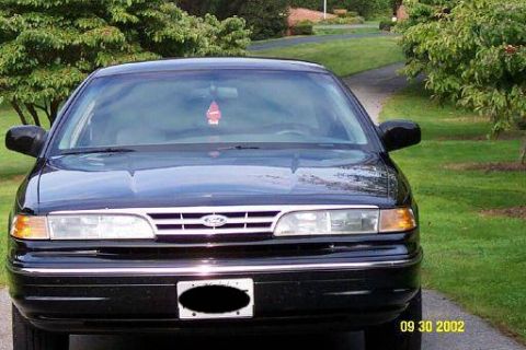 1997 Ford Crown Victoria - Front view of a black Ford Crown Victoria parked on a driveway with trees and grass in the background.