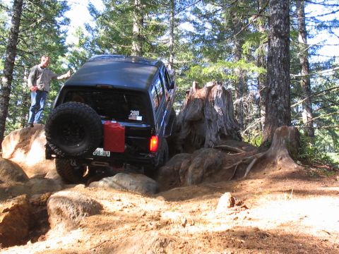1989 Ford Bronco - A black 1989 Ford Bronco tackles a challenging off-road course in a forest setting.