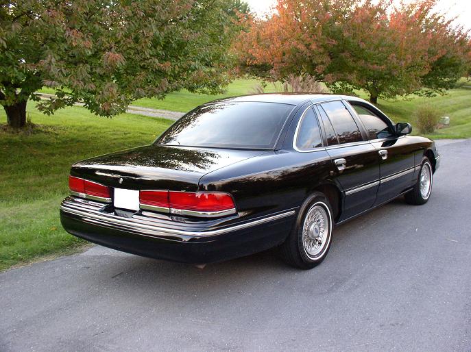 Black 1990s Ford Crown Victoria sedan rear three-quarter view with wire wheels