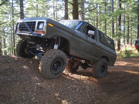 1989 Ford Bronco - This heavily modified Ford Bronco is shown navigating an off-road trail with significant suspension articulation.