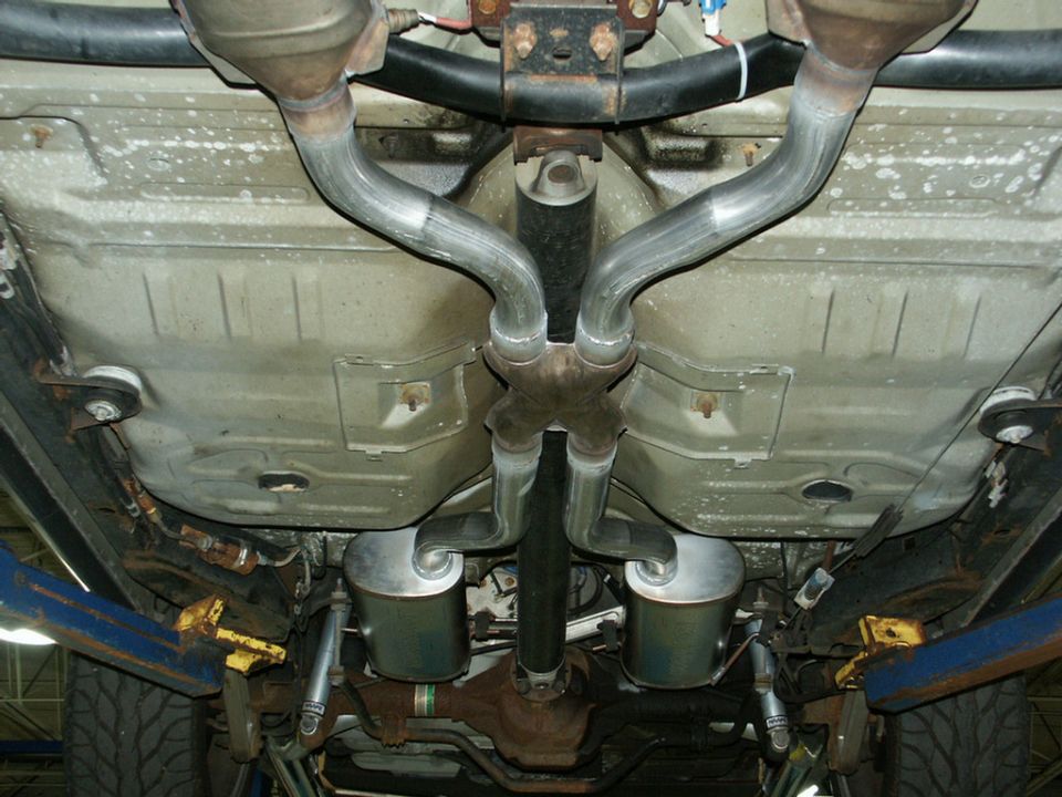 Dual exhaust with X-pipe crossover and chrome mufflers under a sedan on a lift