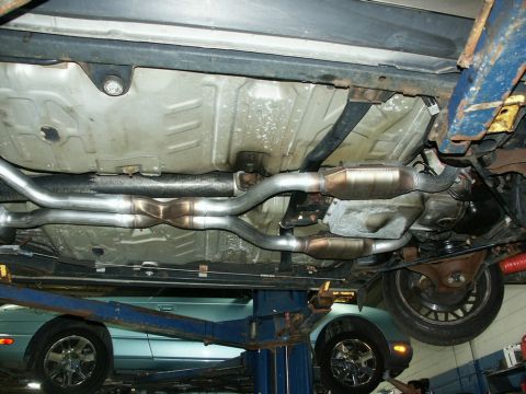 2001 Mercury Grand Marquis - The undercarriage of a vehicle is shown, focusing on its exhaust system, with another car visible on a lift below.