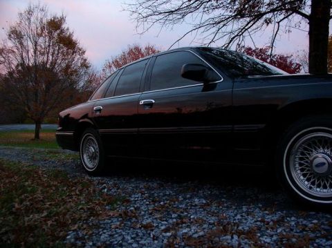 1997 Ford Crown Victoria - A black 1997 Ford Crown Victoria is parked on a gravel surface surrounded by trees in the fall.