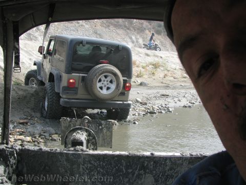 1987 Suzuki Samurai - A tan Jeep Wrangler navigates a muddy off-road course with another vehicle and an ATV visible in the background.